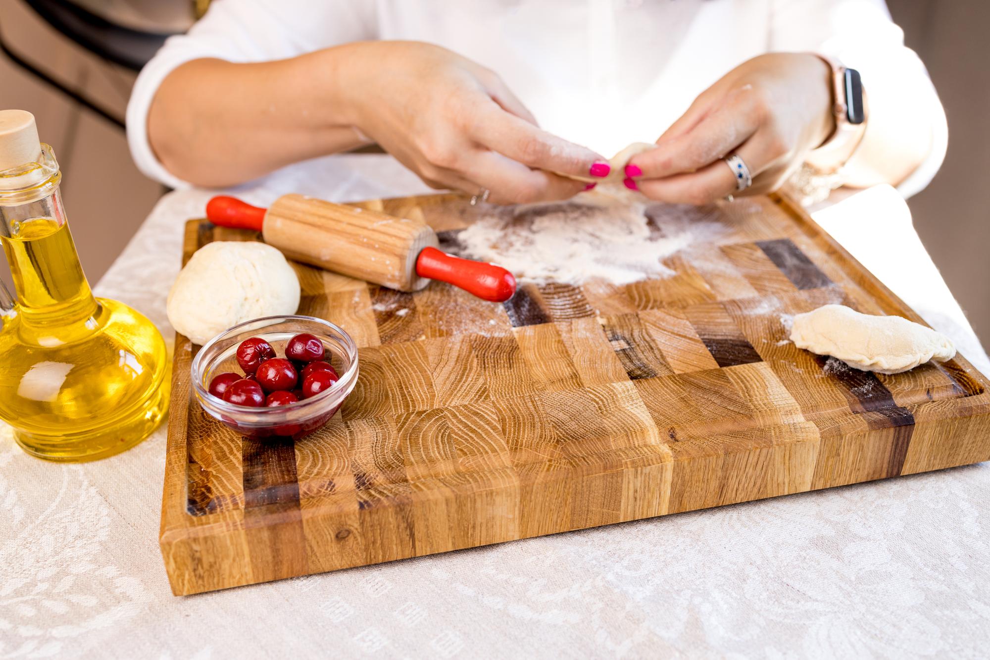 Hands preparing dough on wooden board with herbs